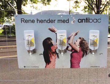 Hygienestasjon på utendørs arrangement: Tre flasker med Antibac hånddesinfeksjon i dispensere montert på en plakat på et gjerde, med teksten "Rene hender med antibac"